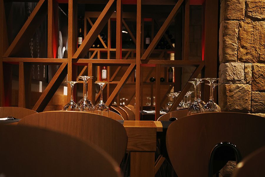 A wooden wine rack, glasses on the tables and a stone wall